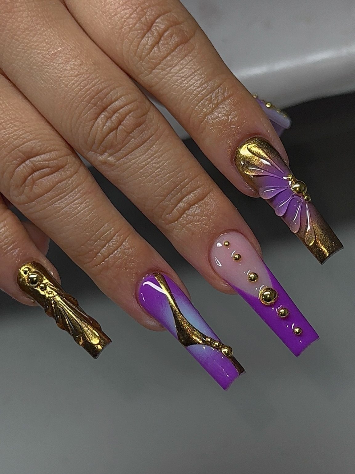 Long purple and gold coffin nails with 3D metallic accents and gold gems.