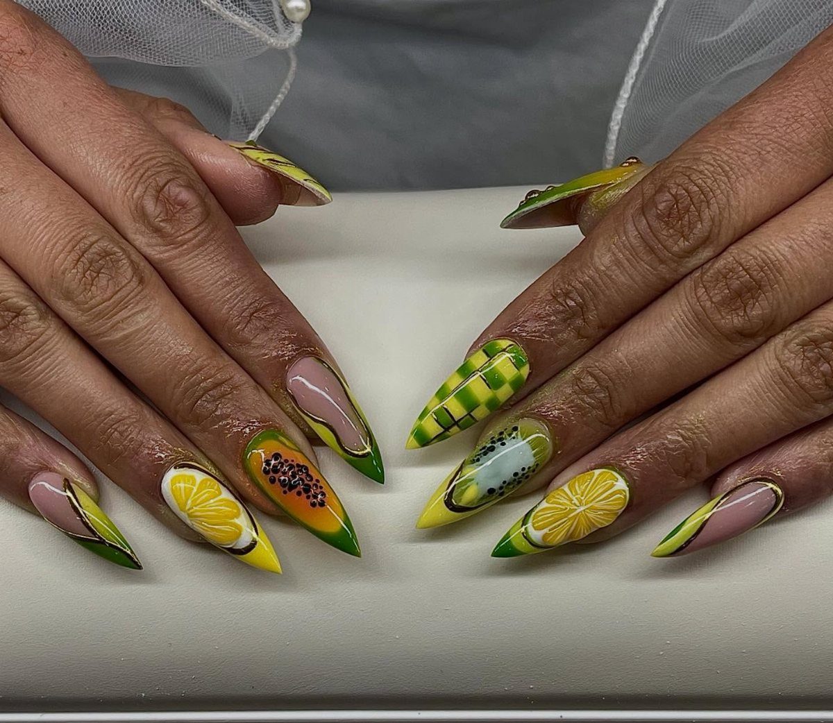 Long pointed nails with lemon art, passion fruit, and yellow grid patterns.