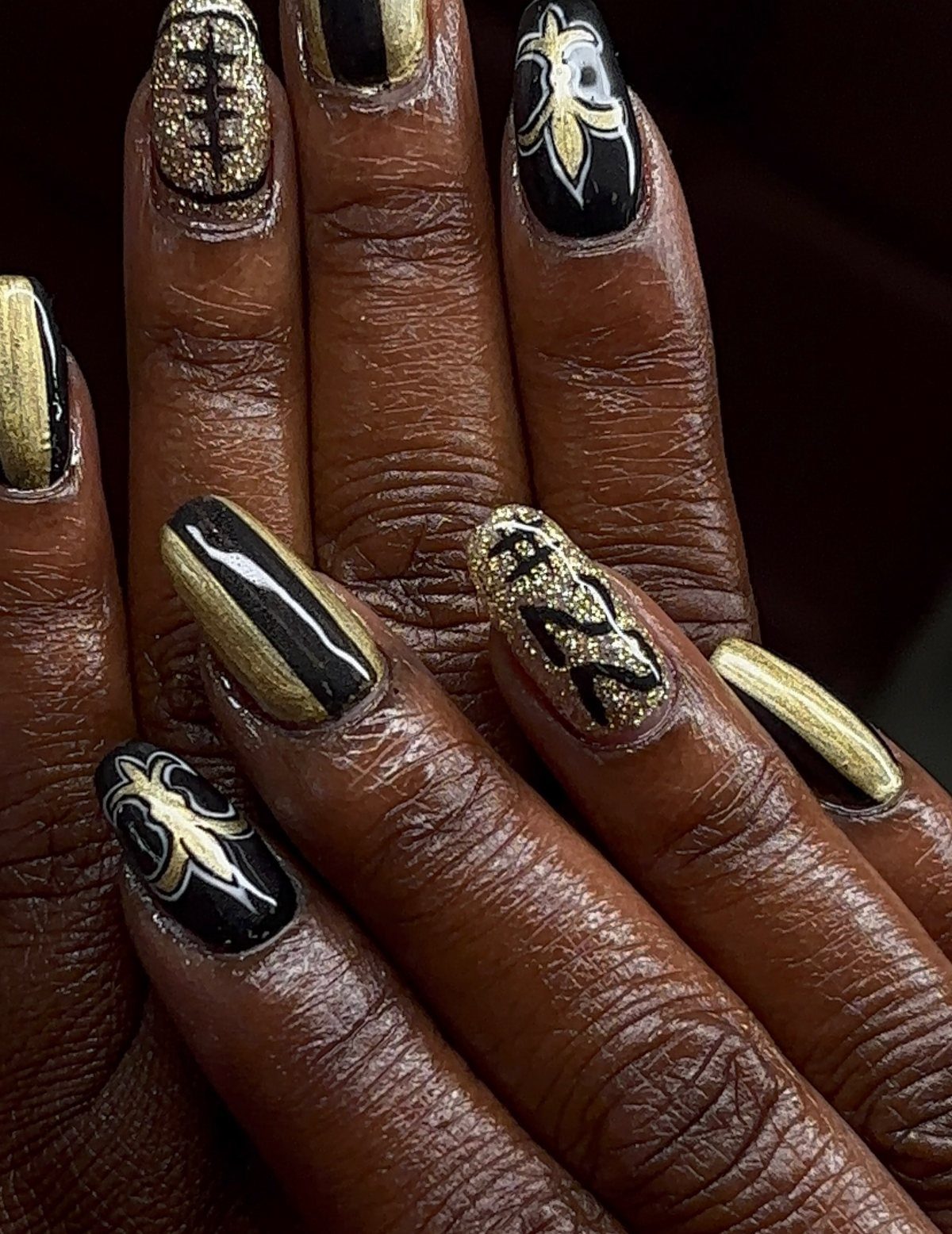 Black and gold nail art featuring a fleur-de-lis and a glittery football.
