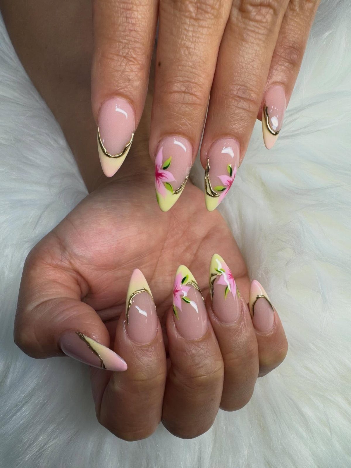 Almond-shaped nails with yellow tips, gold swirls, and small pink painted flowers.