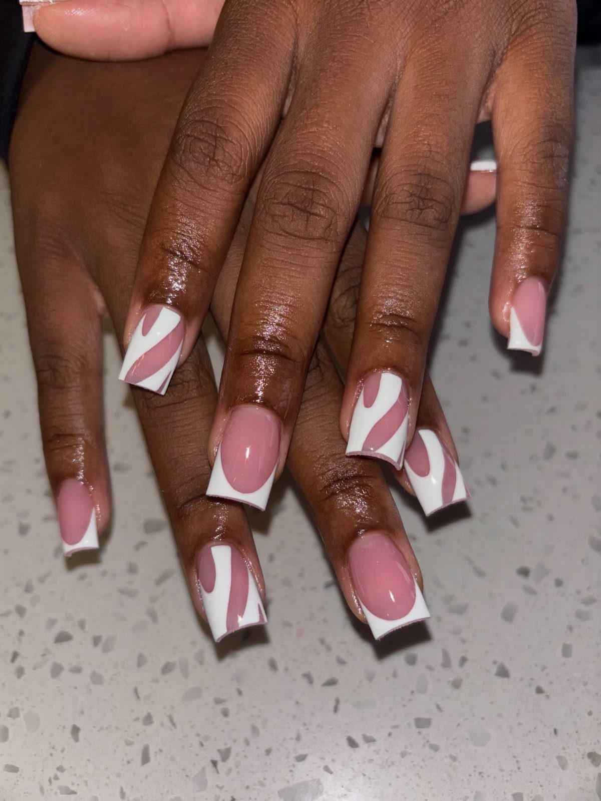 Pink and white square nails with swirling patterns and French tips on dark skin.