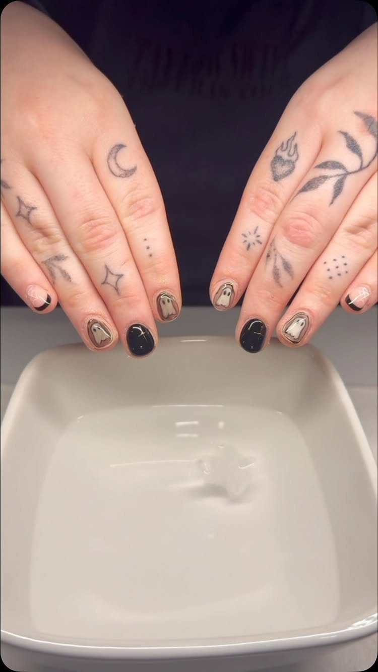 Tattooed hands featuring nail art with tiny white ghosts and black polish.