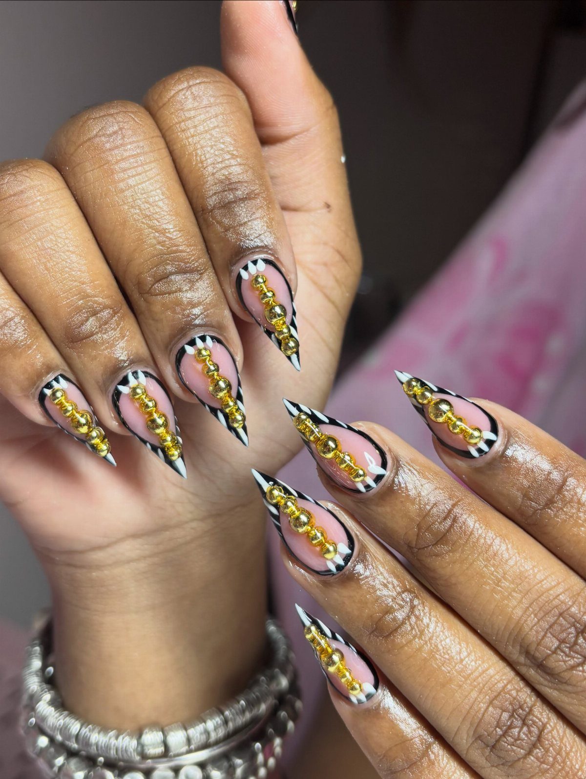 Long pointed nails with pink base, black and white patterns, and gold beads.