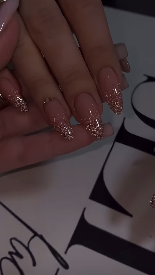 Almond-shaped nails with a nude base and rose gold glitter ombré tips.
