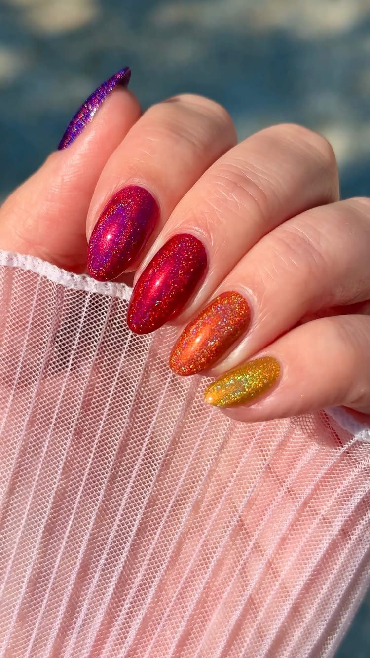 Glittery gradient nails in purple, red, orange, and yellow on a hand.