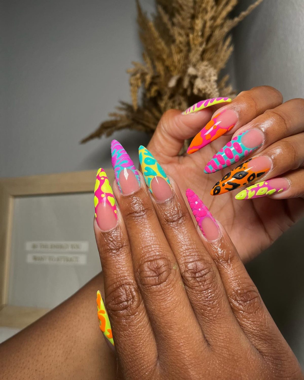 Long almond nails with neon pink, orange, yellow, and blue abstract wavy swirls.