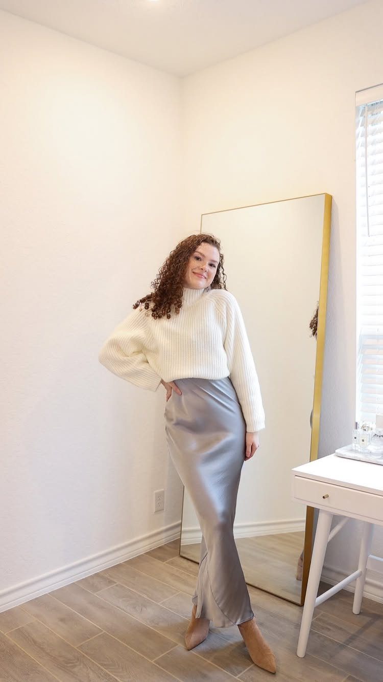 Woman wearing a white crew neck jumper and silver satin slip skirt.