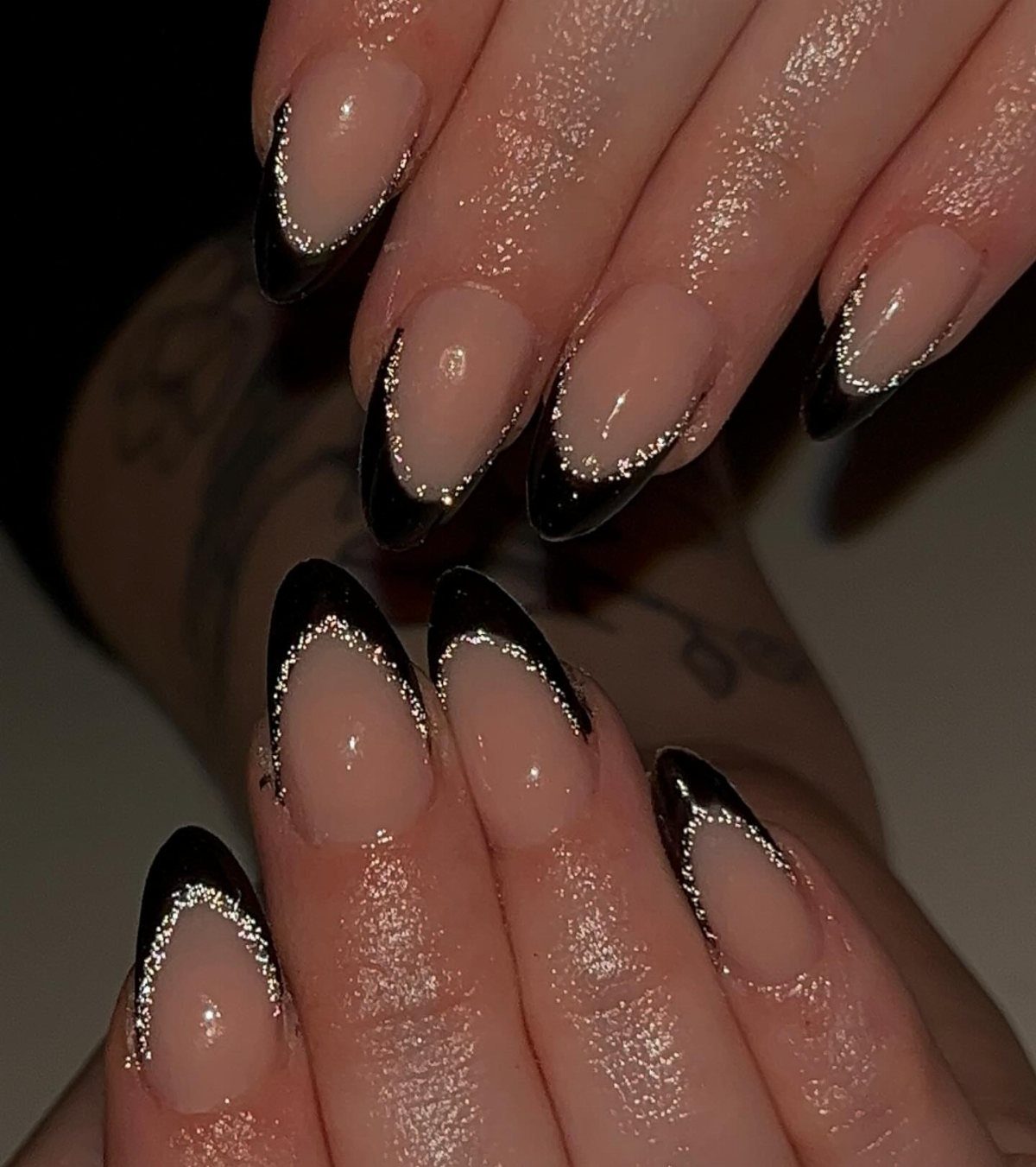 Almond-shaped nails with nude bases, black tips, and silver glitter accent lines.