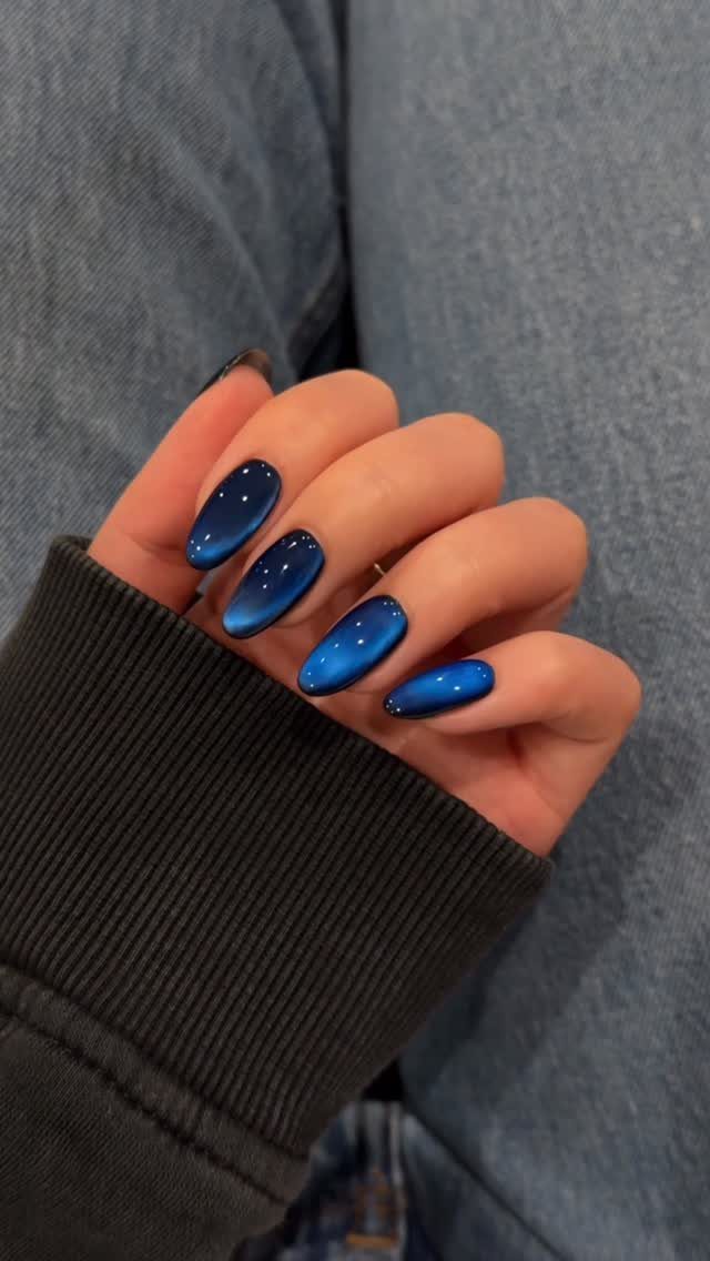 Deep blue cat-eye nails with a shimmering light effect on oval-shaped tips.