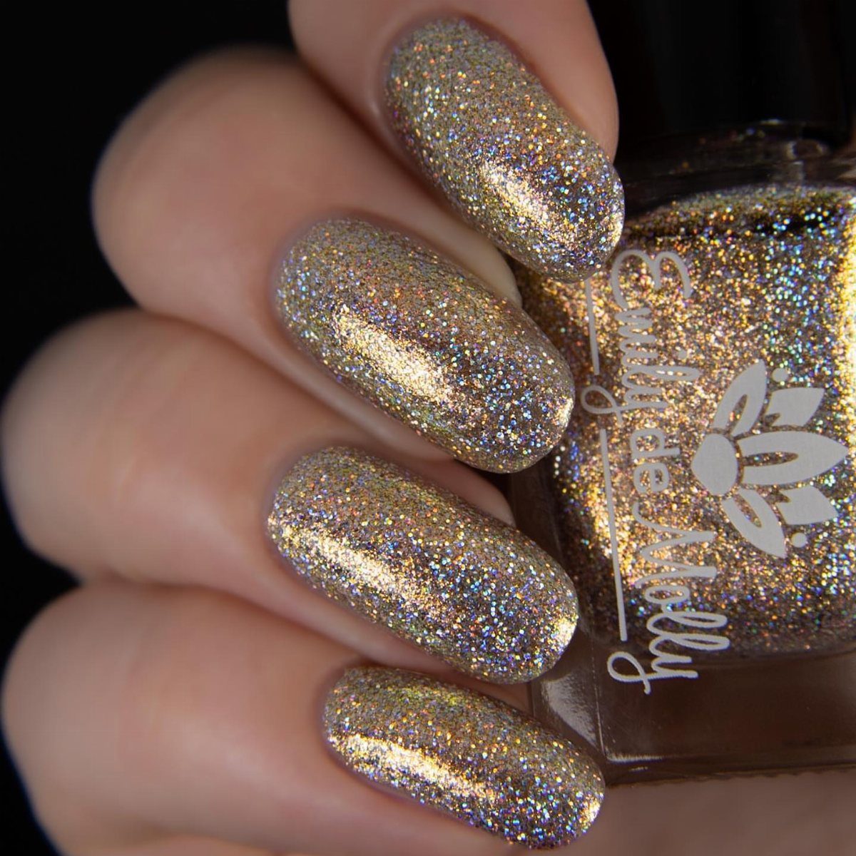 Holographic gold glitter nails holding a matching bottle of nail polish.