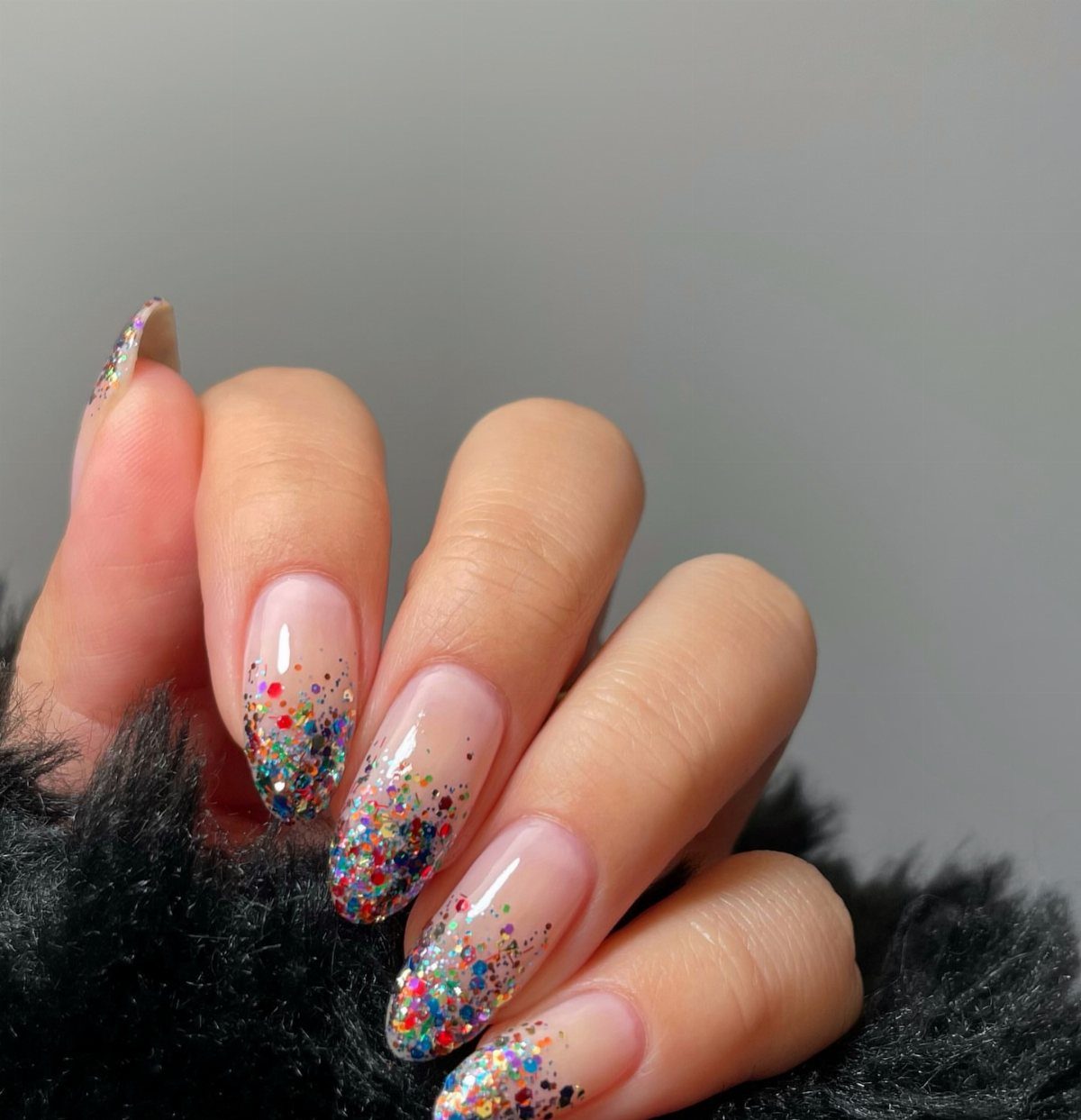 Almond-shaped nails with sheer nude base and multicolored confetti glitter on the tips.