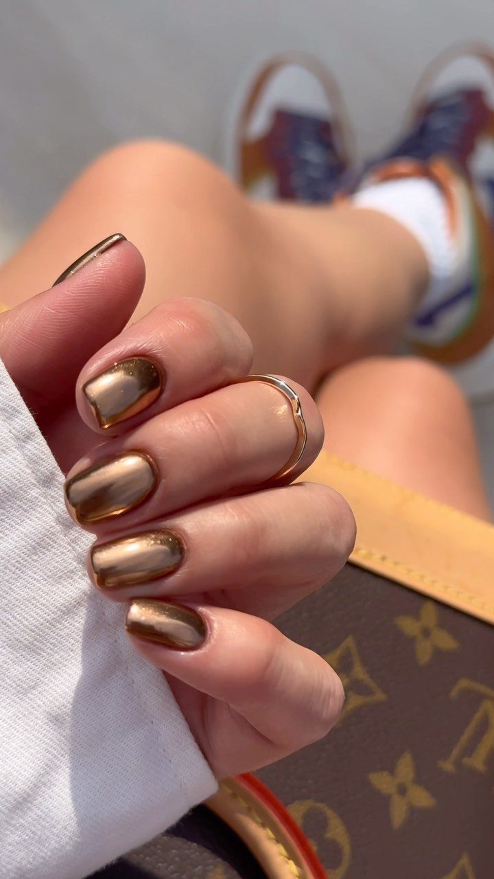 Copper chrome metallic nails on a hand resting on a luxury brown bag.