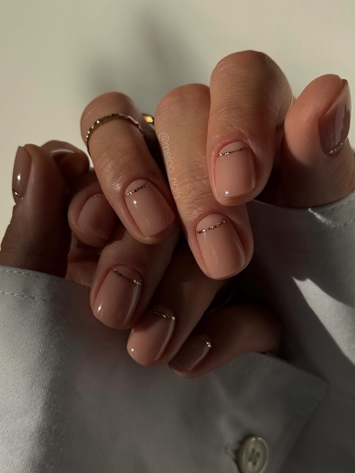 Nude nails with a thin gold glitter line across the base of each nail.
