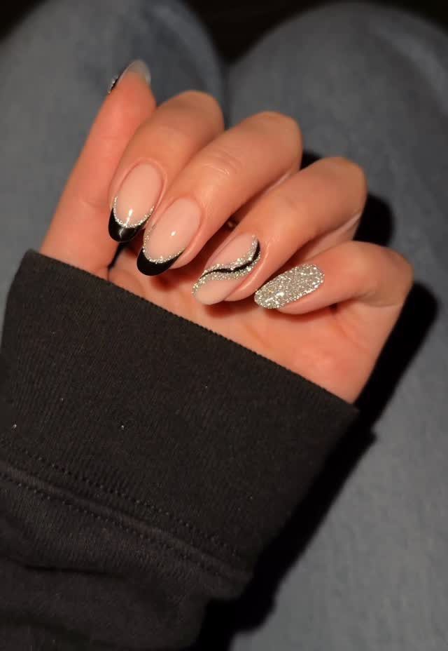 Almond-shaped nails with nude base, black tips, silver glitter accents, and one glitter nail.