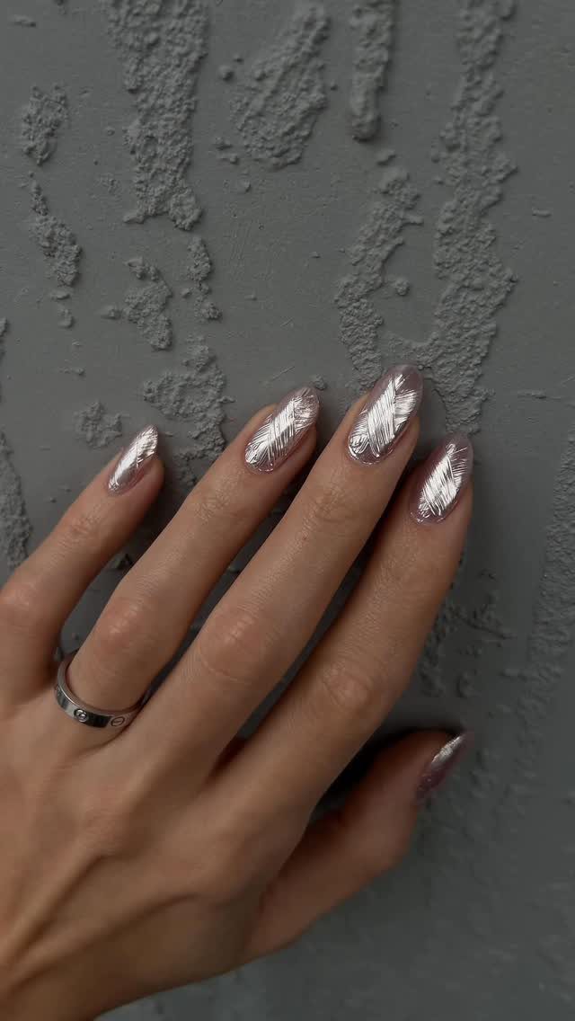 Hand with 3D textured silver metallic nails posed against a grey textured wall.