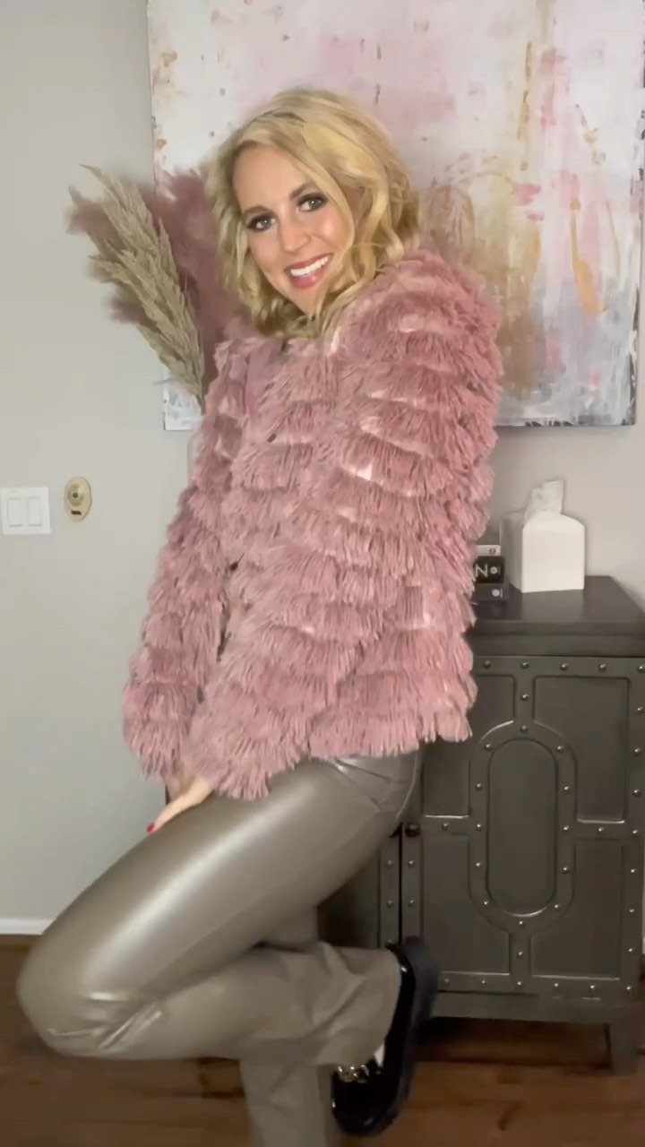 Blonde woman wearing a pink shaggy jacket and metallic silver leggings posing indoors.