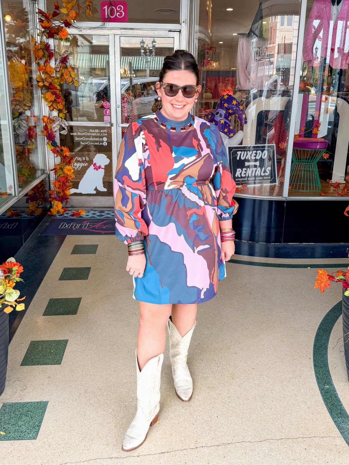 Woman in a colorful abstract print dress and white cowboy boots standing outdoors.