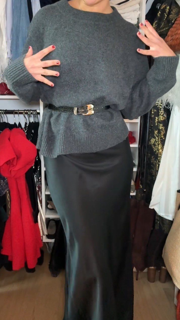 Person wearing a grey sweater with a black belt and black satin slip skirt.
