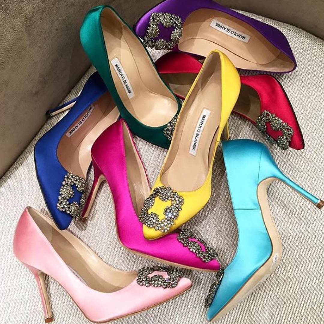 Colorful satin high-heel pumps with crystal buckles arranged on a neutral fabric surface.