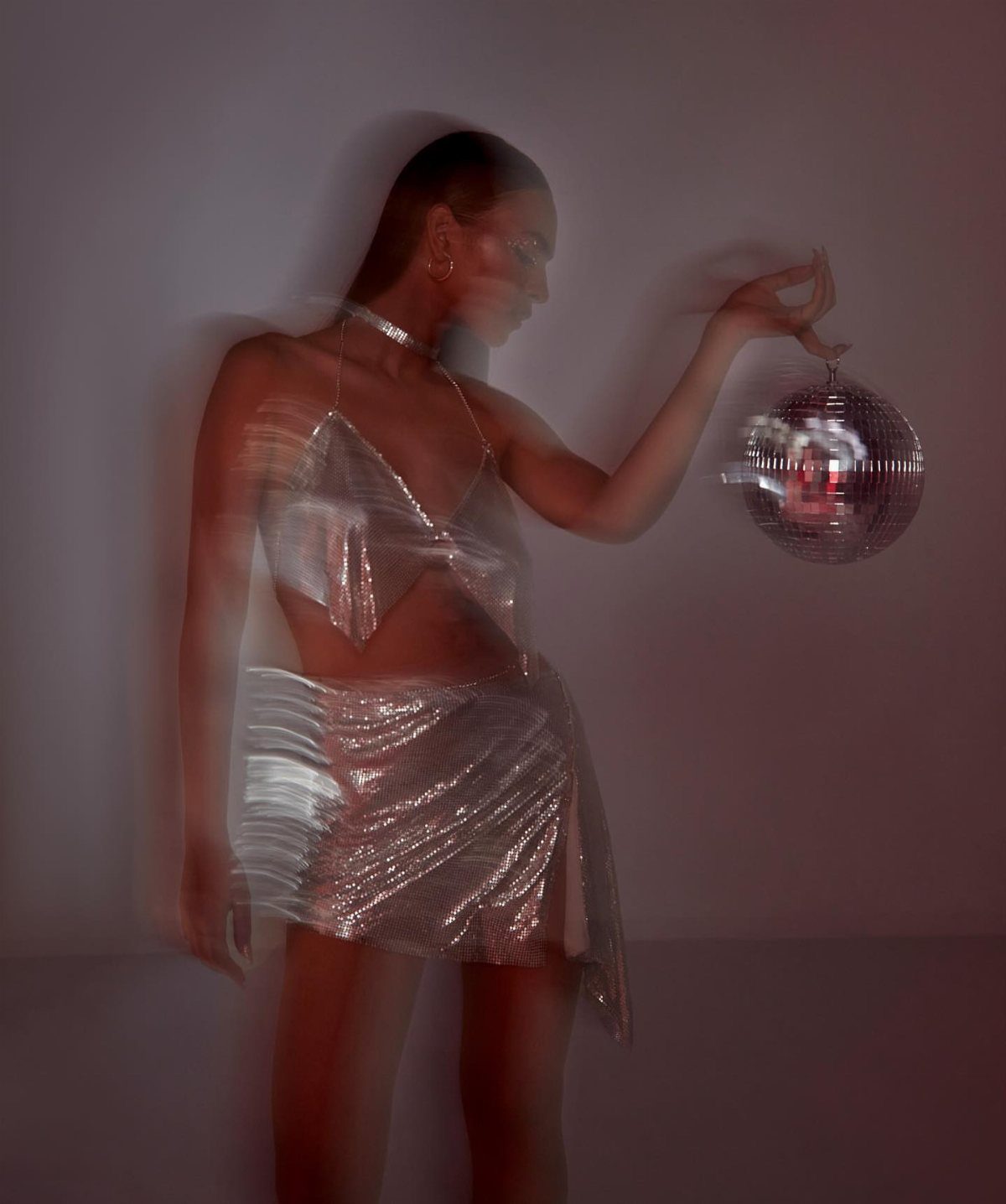 Woman in a shimmering silver two-piece outfit holding a disco ball