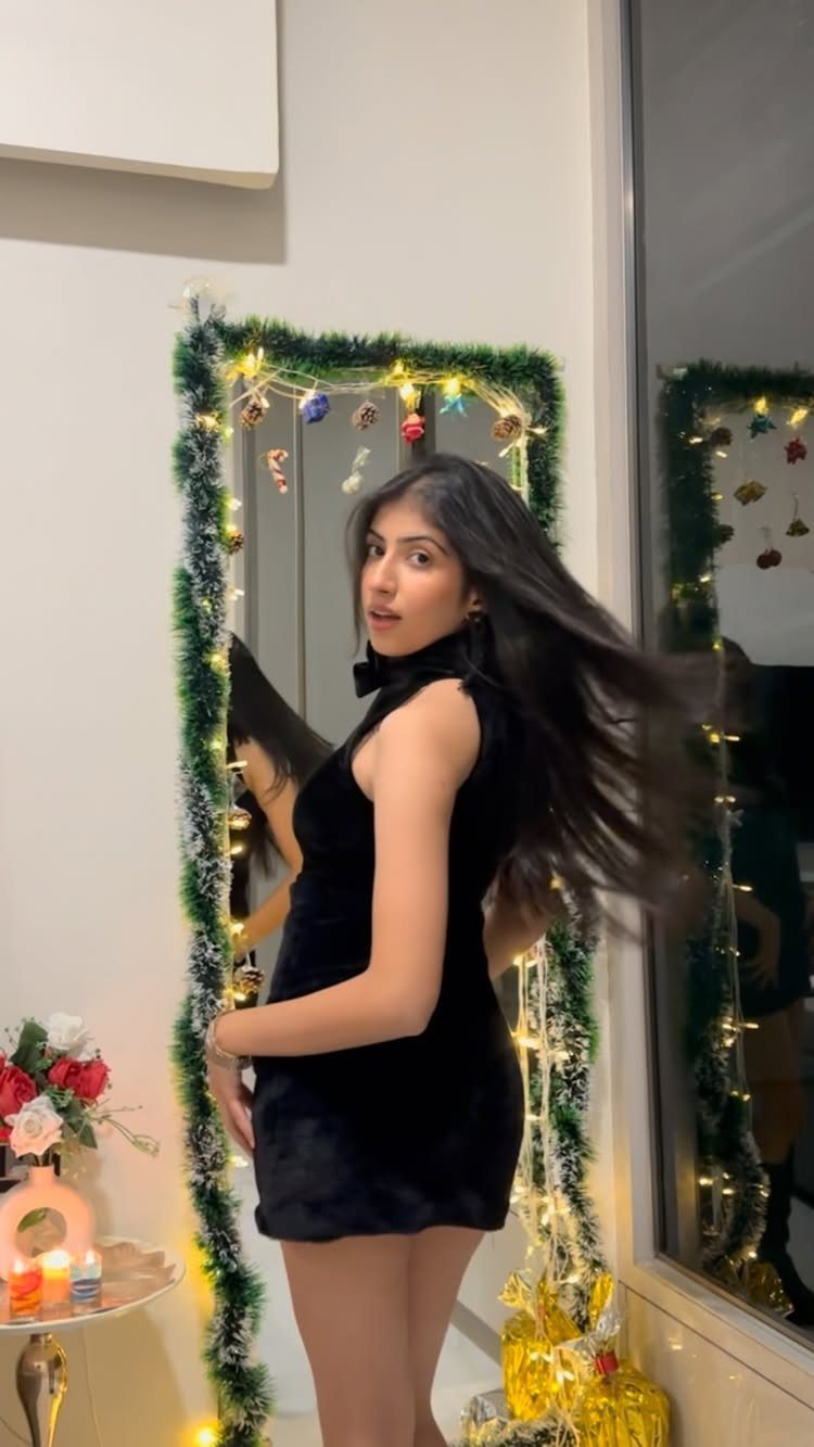 Woman wearing a short black velvet dress posing by a decorated mirror.