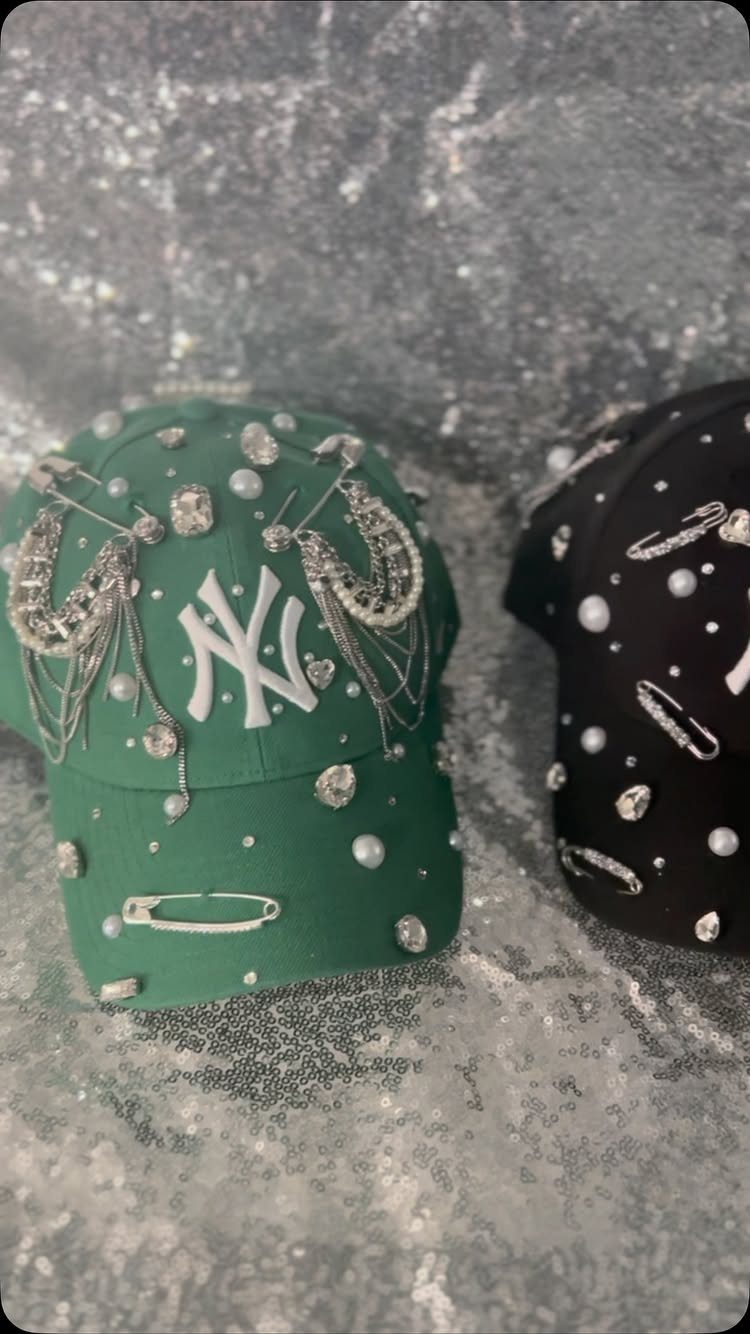 Two embellished baseball caps with rhinestones and pearls on a silver glitter background