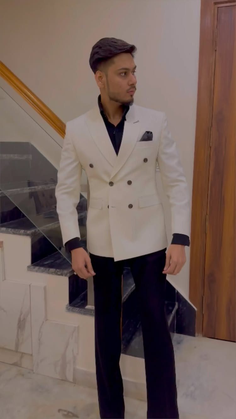 Man in a white double-breasted blazer and black trousers standing by a staircase.