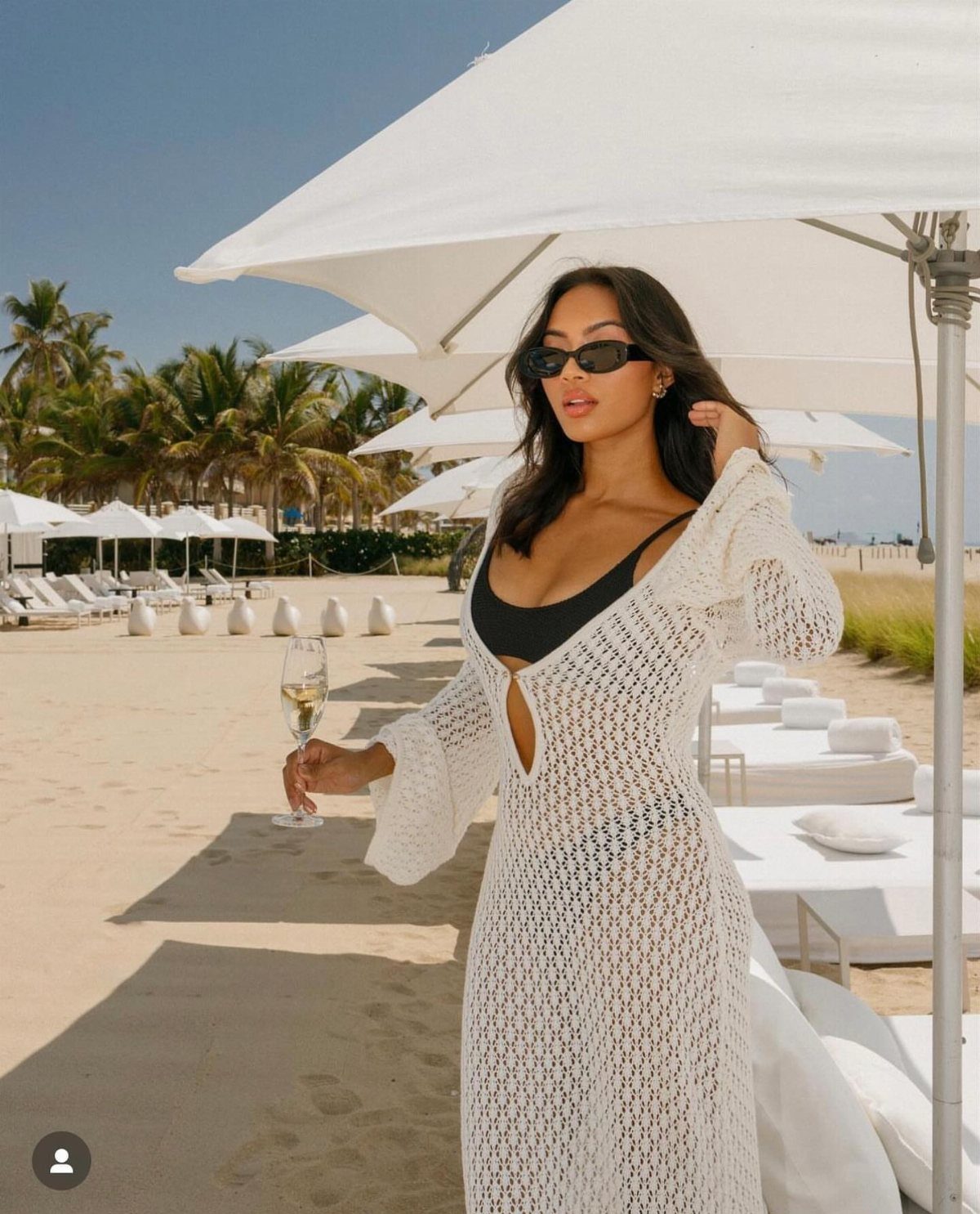 Woman wearing a white crochet cover-up over a black bikini on a beach.