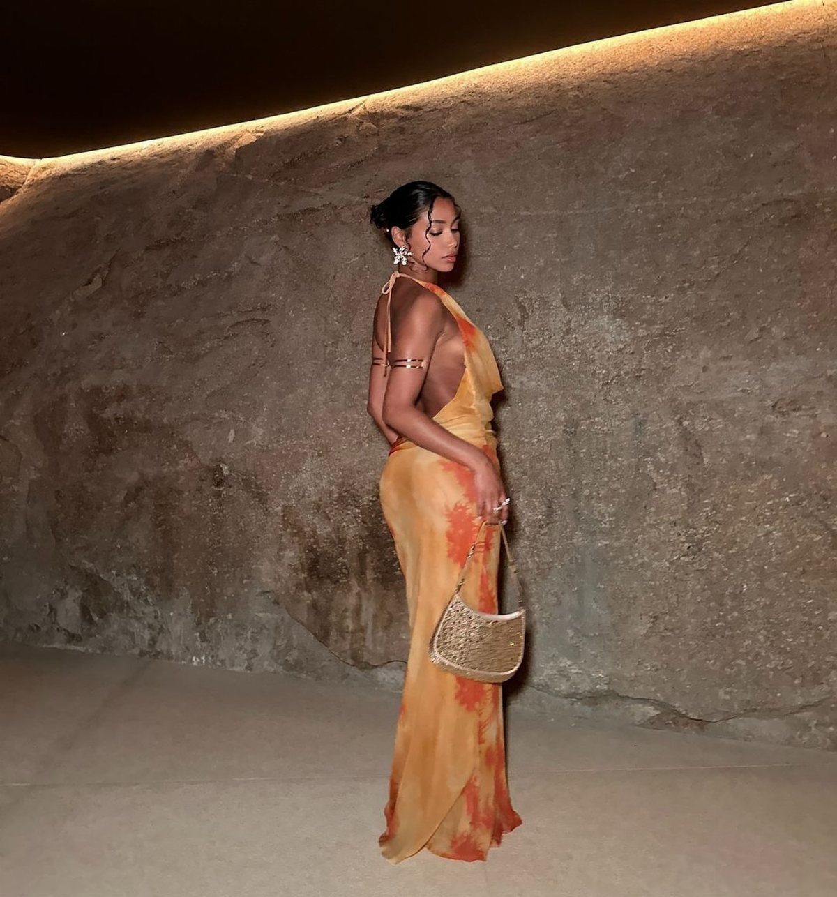 Woman in an orange gradient maxi dress holding a gold beaded handbag.