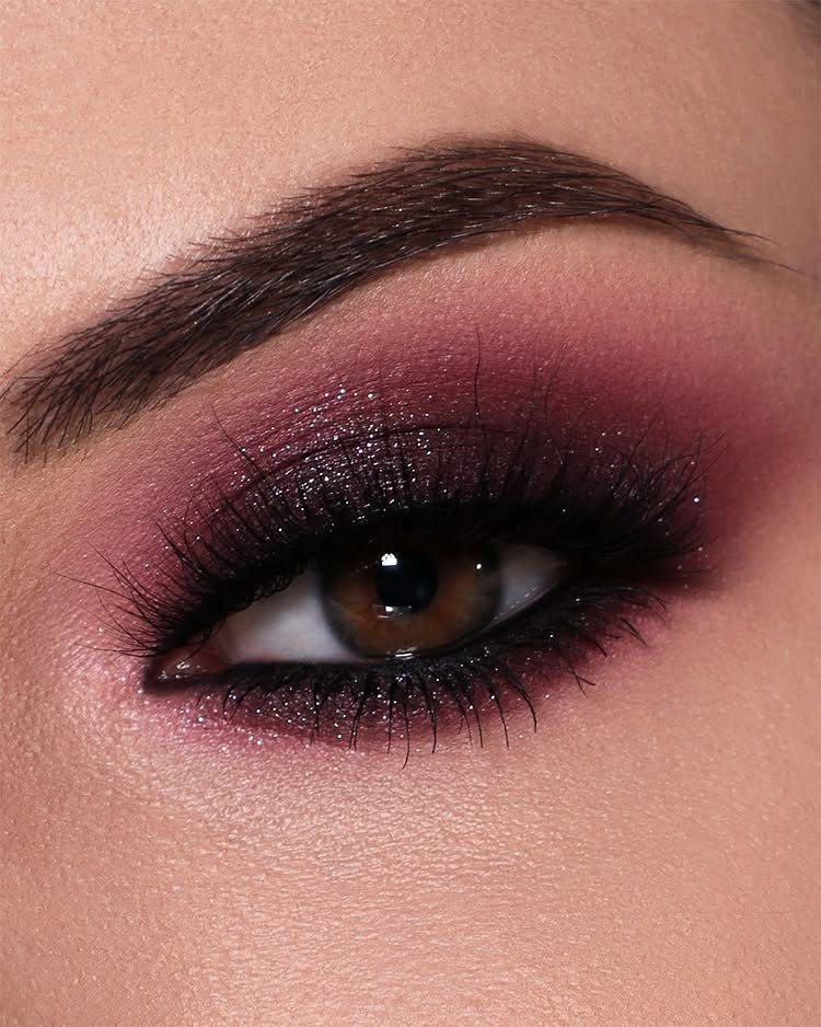 Close-up of eye with shimmering burgundy and purple eyeshadow and long lashes.