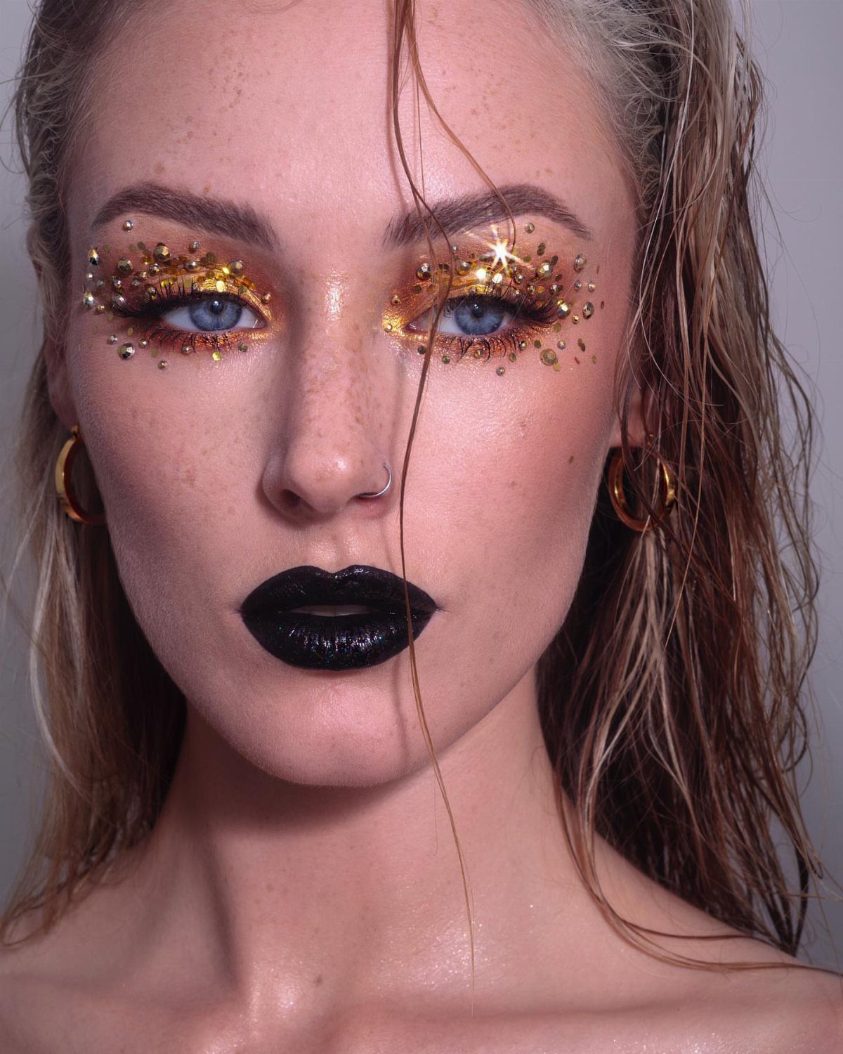 Woman with gold glitter eye makeup and bold black lips posing for portrait