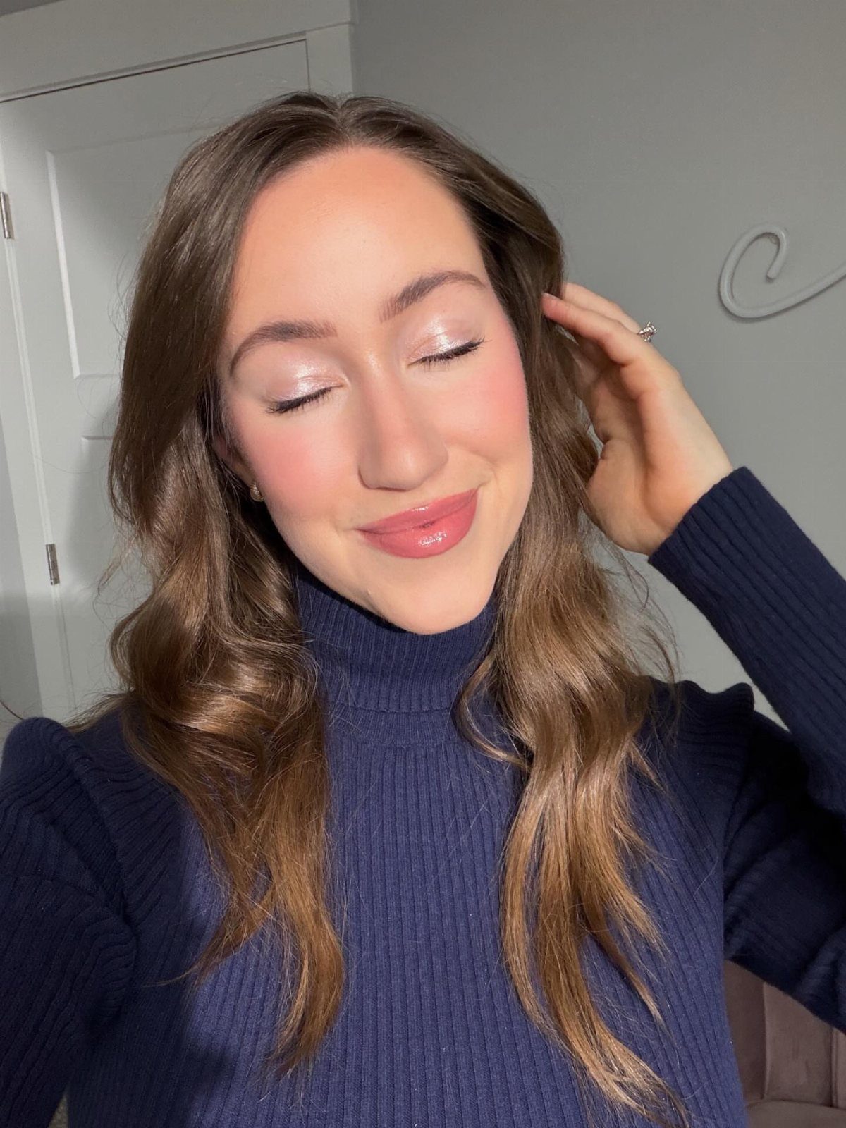 Woman with shimmering inner corner eyeshadow and highlighted cheeks wearing a navy turtleneck.
