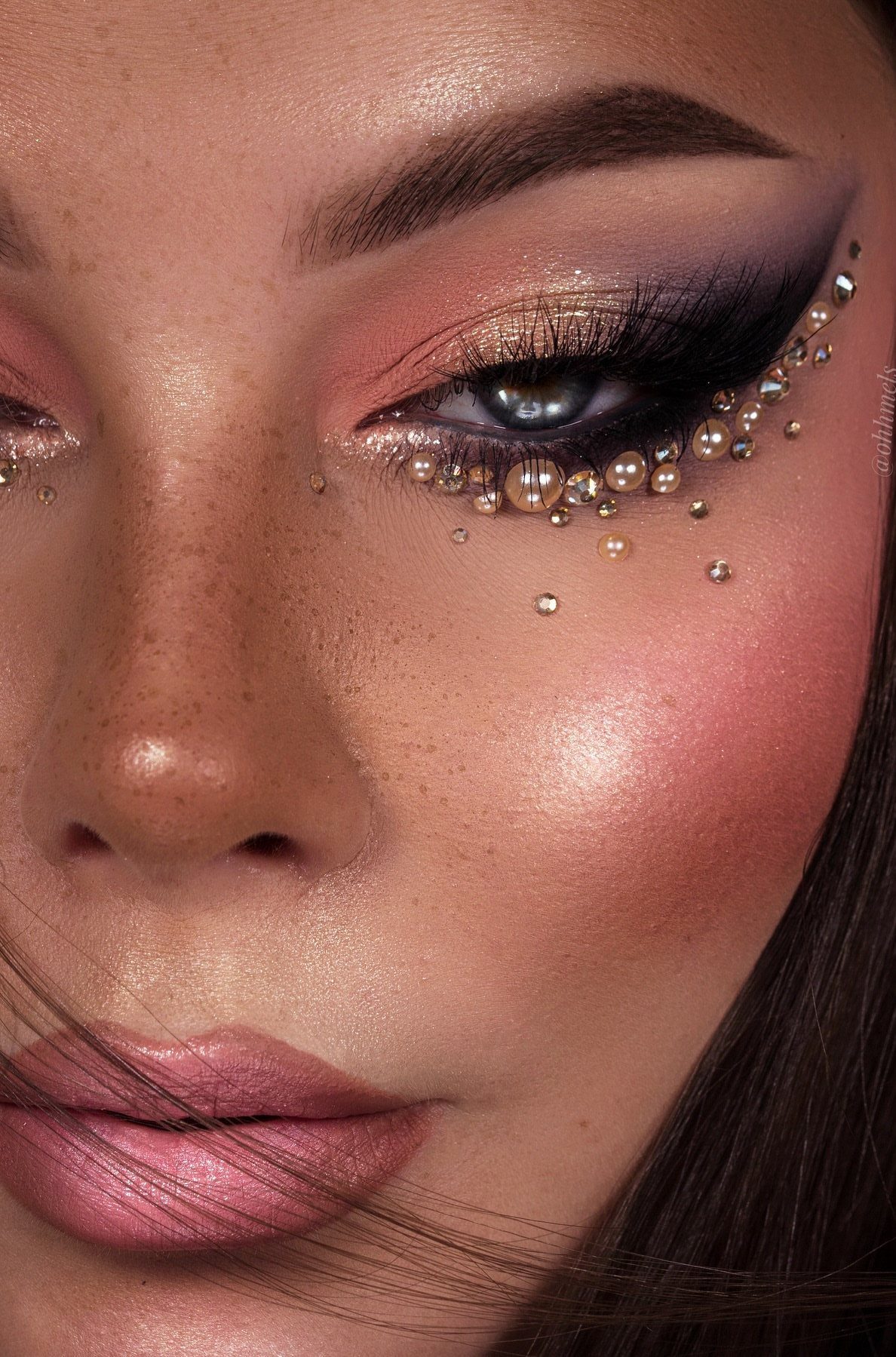 Woman with glamorous eye makeup featuring pink eyeshadow and decorative pearls around eyes.