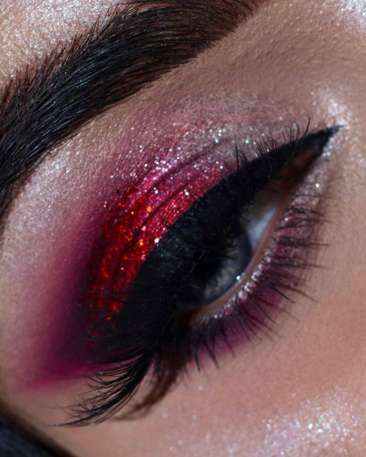 Eye with red glitter eyeshadow, sharp black winged eyeliner and silver shimmer highlights.