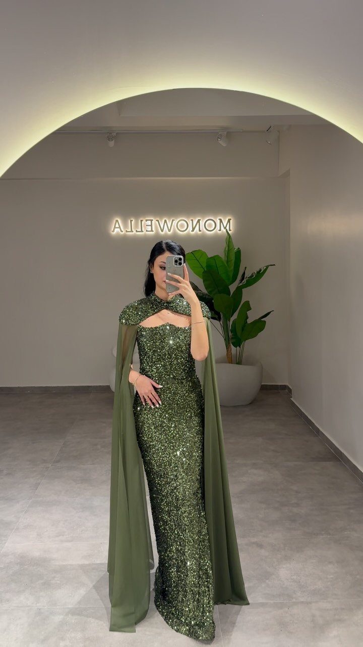 Woman in olive green sequined maxi gown with attached cape and cutout neckline.