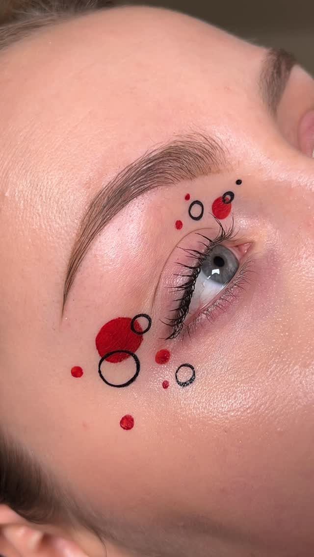 Eye makeup featuring abstract red and black circles and dots around the eyelid.