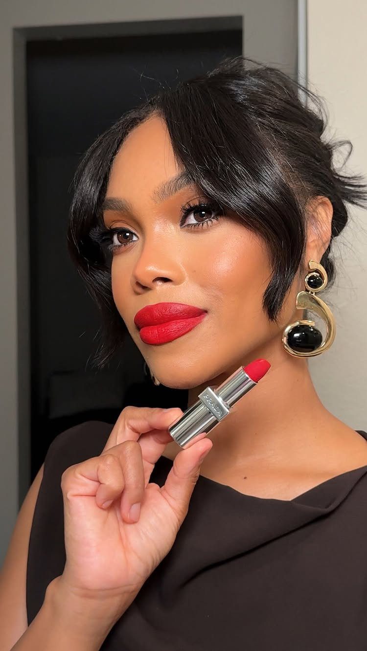 Woman with bold red matte lipstick holding a matching lipstick tube.