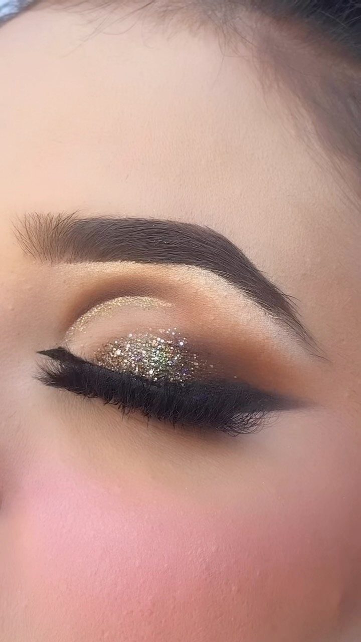 Eye makeup with gold glitter eyeshadow, winged eyeliner, and long false lashes.