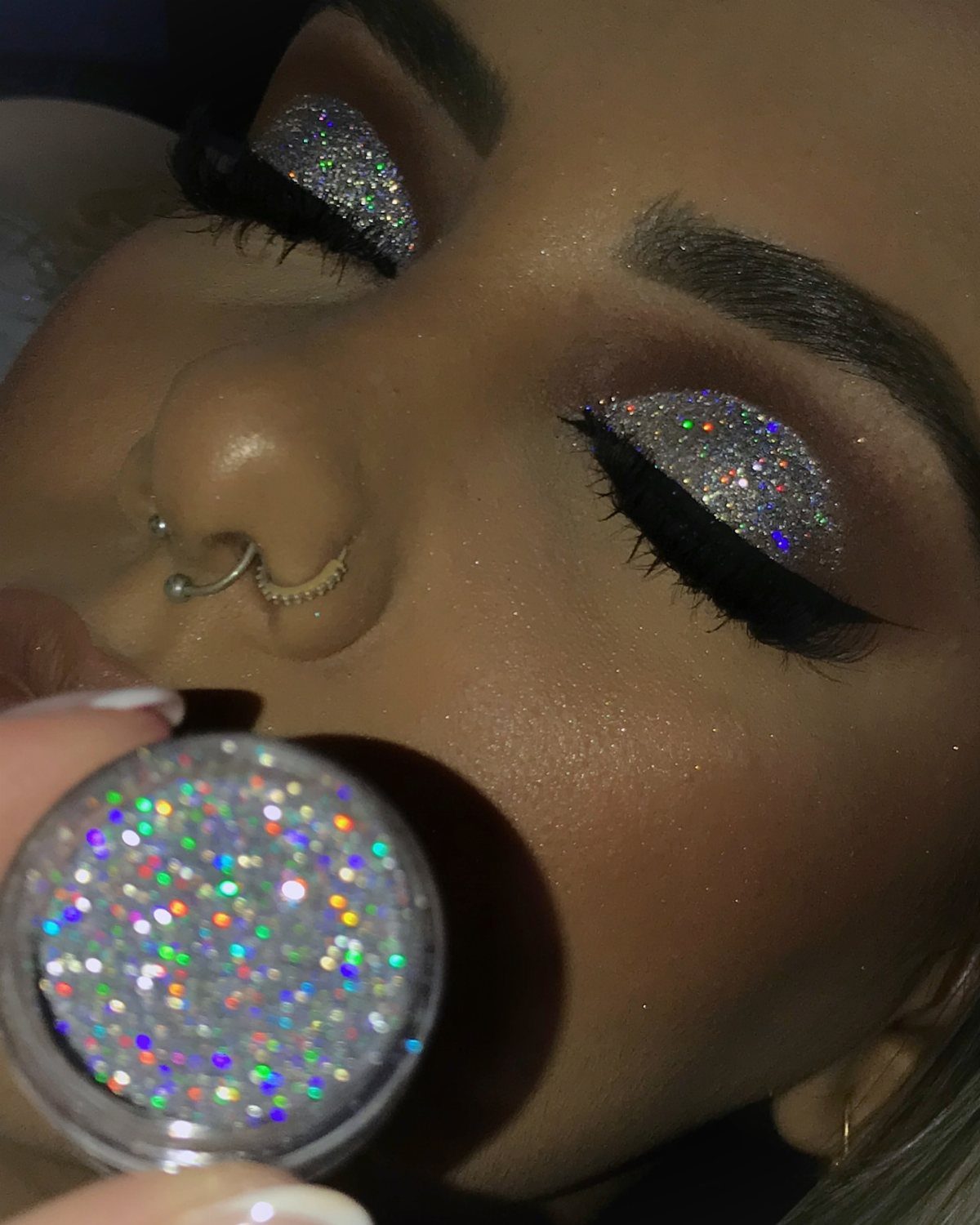 Person with holographic glitter smoky eye makeup holding a pot of iridescent glitter.