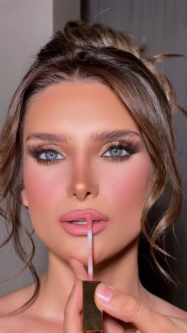 Woman with glowing skin and matte pink lips applying lipstick with a wand.