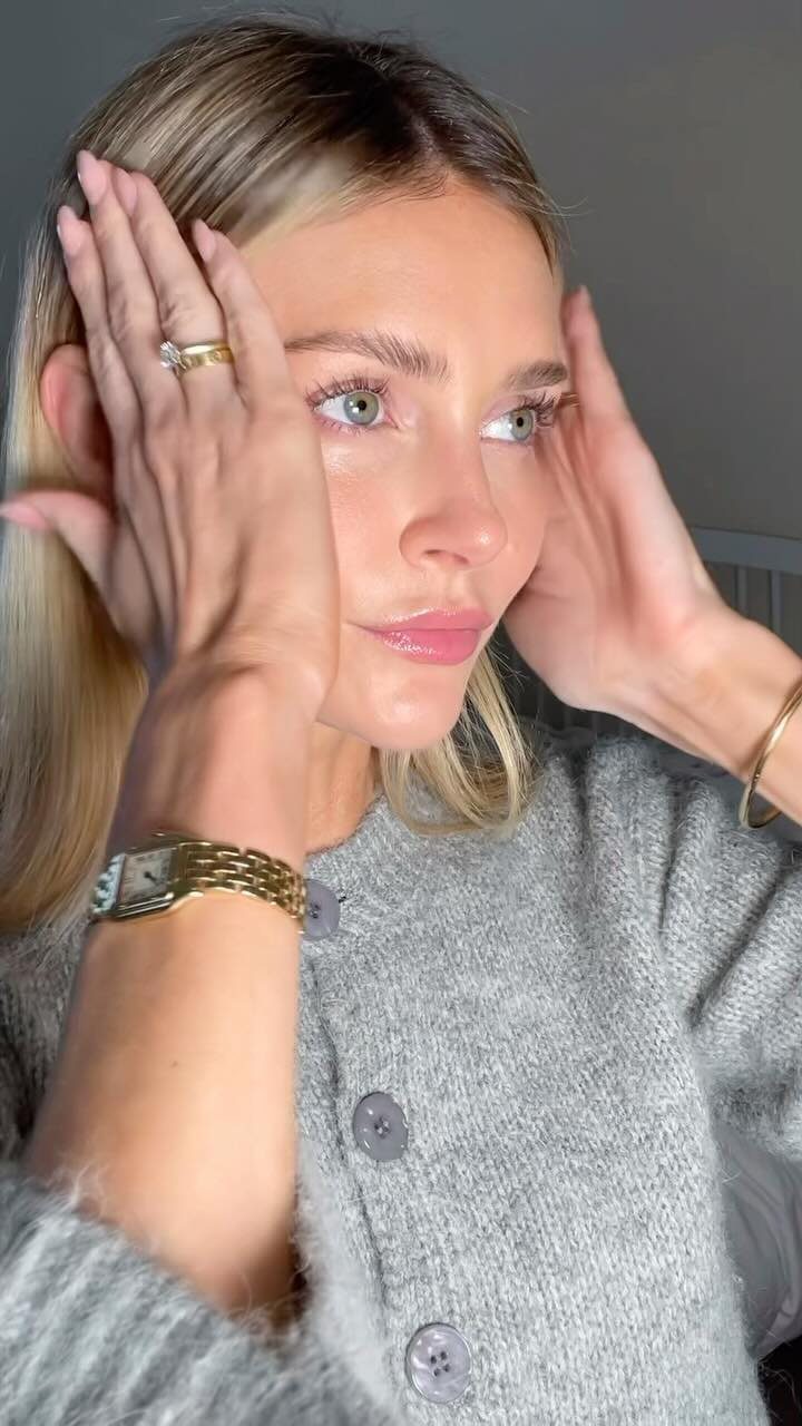 Blonde woman with soft glam makeup wearing a grey knit cardigan and gold jewelry