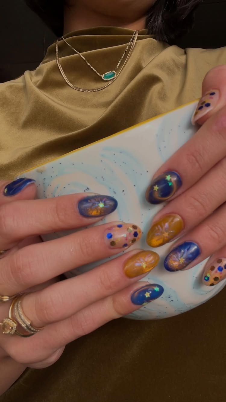 Manicured nails with blue and gold celestial designs holding a ceramic bowl.