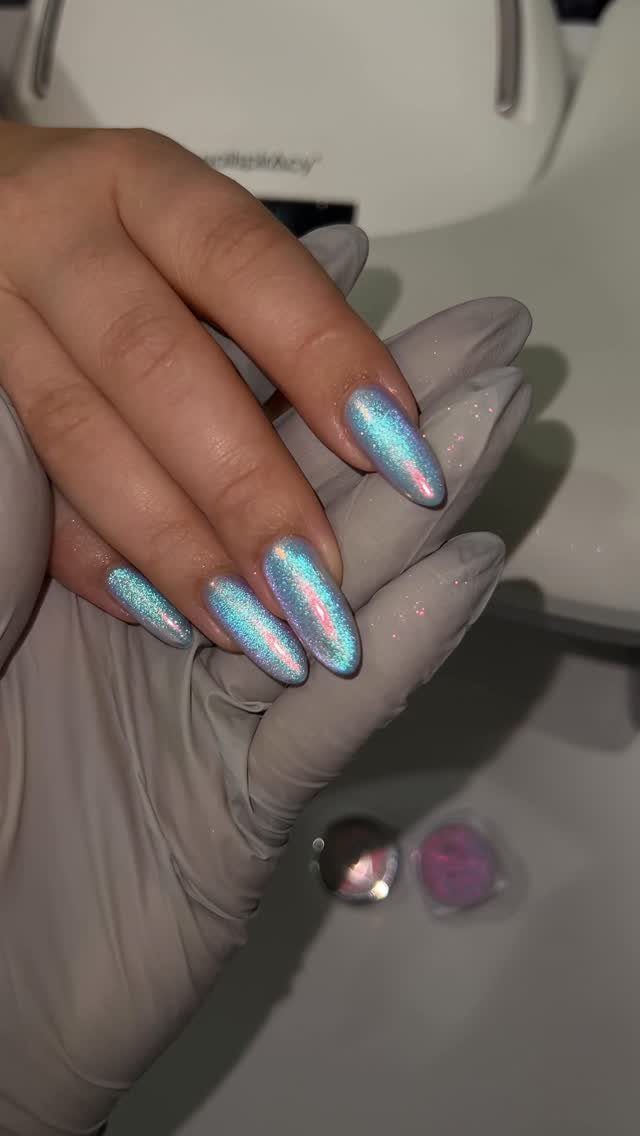 Iridescent blue and silver chrome almond-shaped nails resting on a gloved hand.