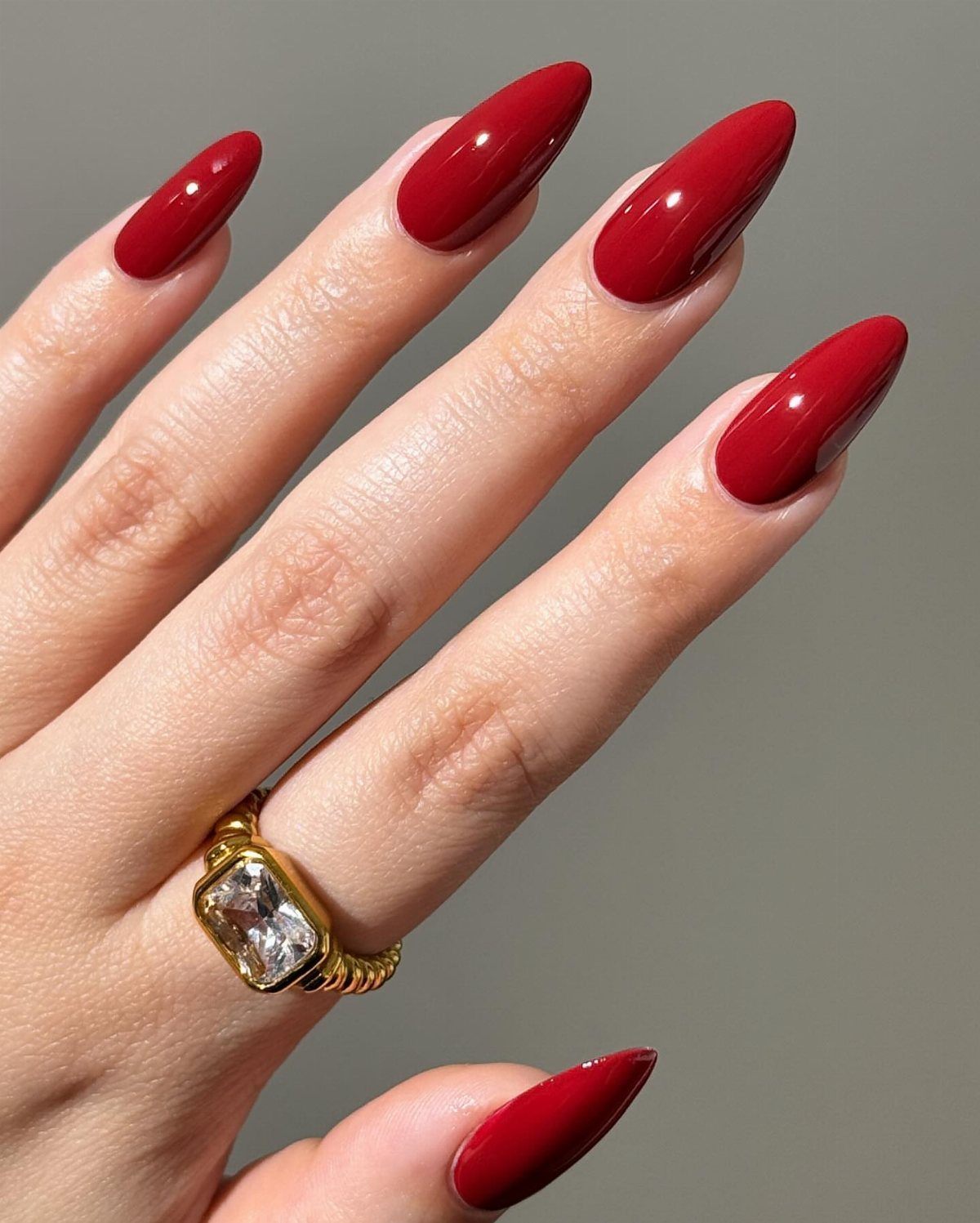 Almond-shaped nails painted glossy red with a gold gemstone ring on a finger.