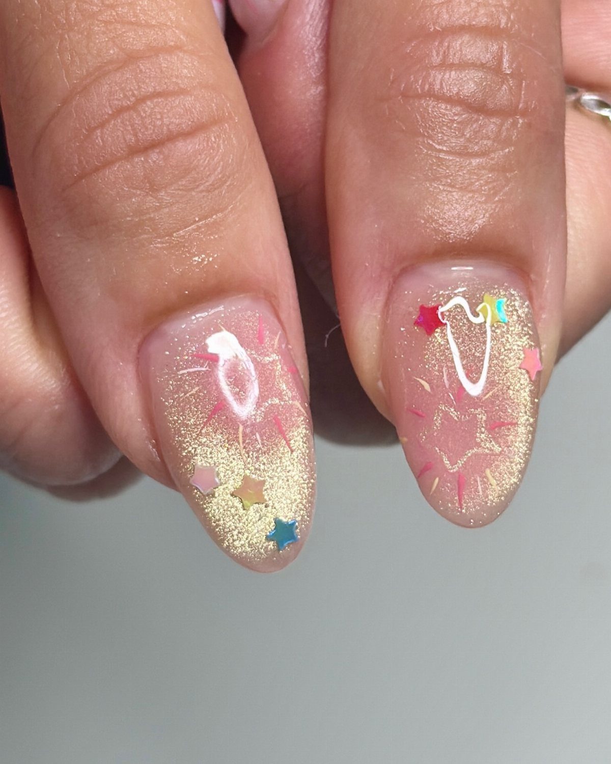 Fingernails with pink polish, gold glitter gradients, and colorful star sequins.