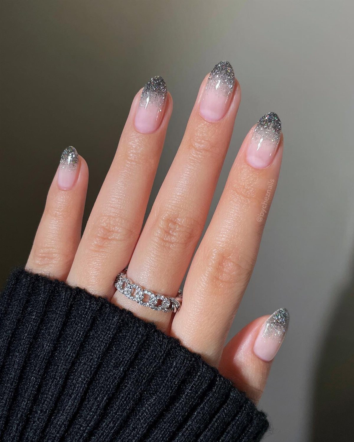 Hand with silver glitter gradient nails and a diamond ring wearing black sweater
