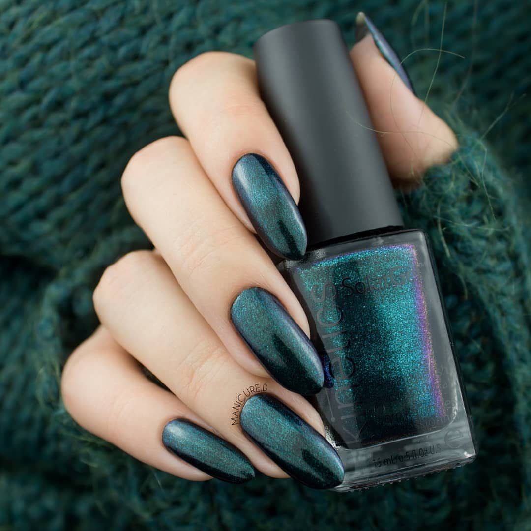 Teal-green metallic nails holding a matching bottle of polish against a green sweater