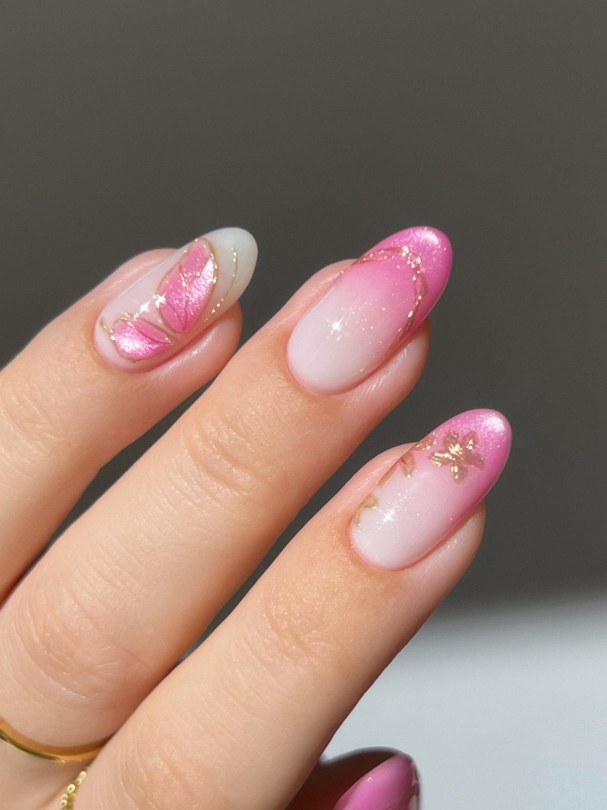 Almond-shaped nails with pink and white ombre, iridescent swirls, and gold accents.