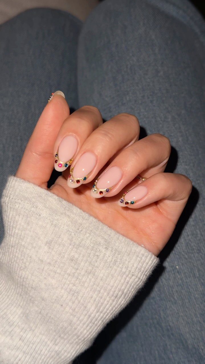 Nude almond nails with colorful rhinestones placed along the cuticle line.