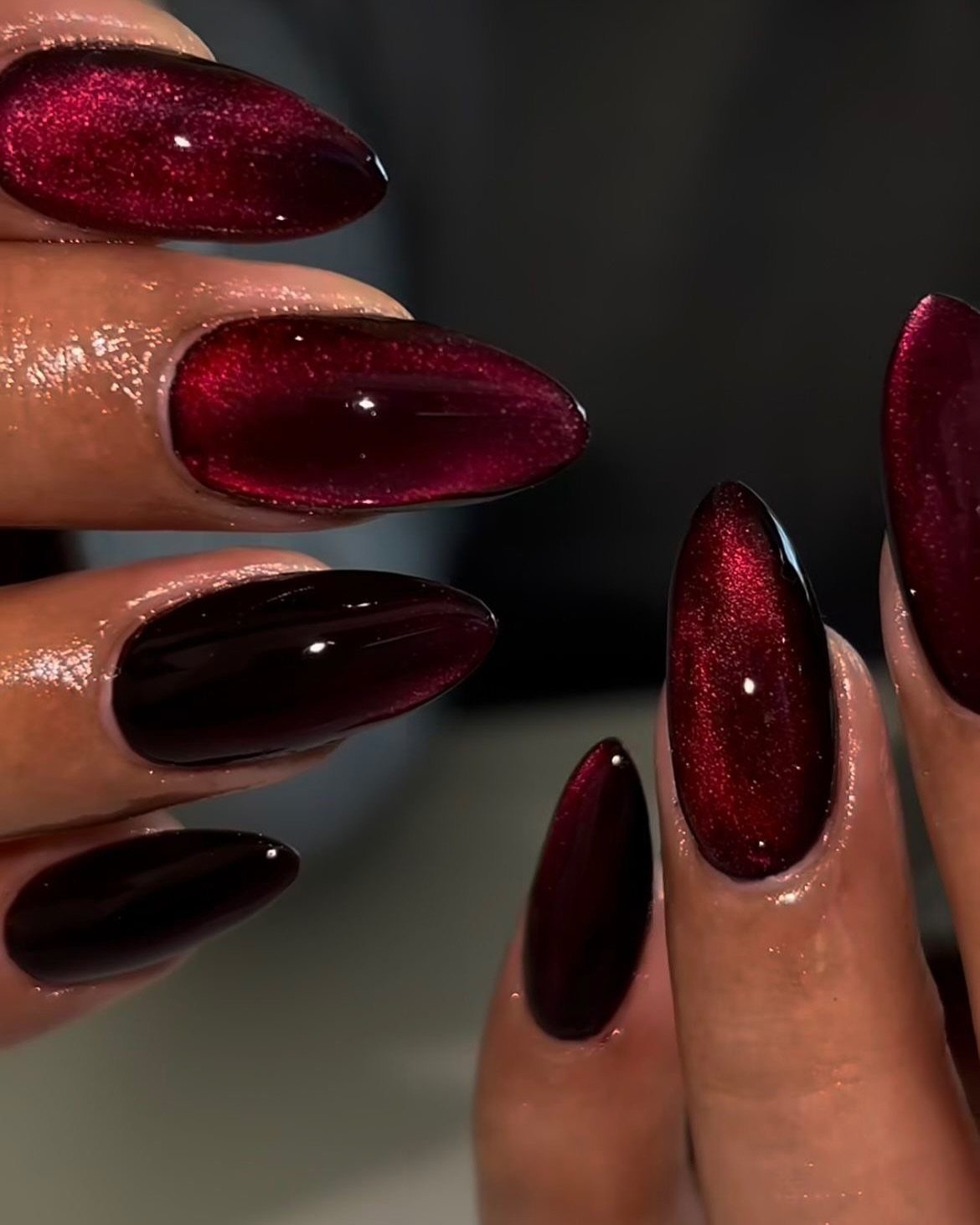 Almond-shaped nails with deep red shimmering velvet effect polish on a hand.